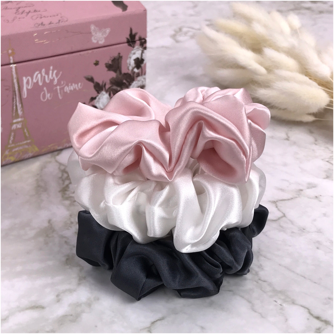 Celestial Silk large charcoal ivory and pink silk scrunchies stacked on marble counter with plant and a jewelry box in the background