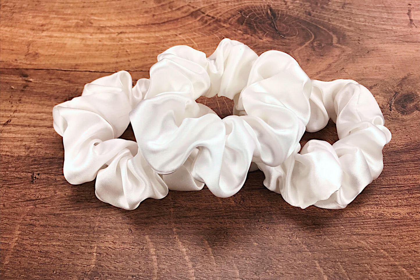 Large undyed ivory silk hair ties by Celestial Silk laying in a pile on a wood vanity