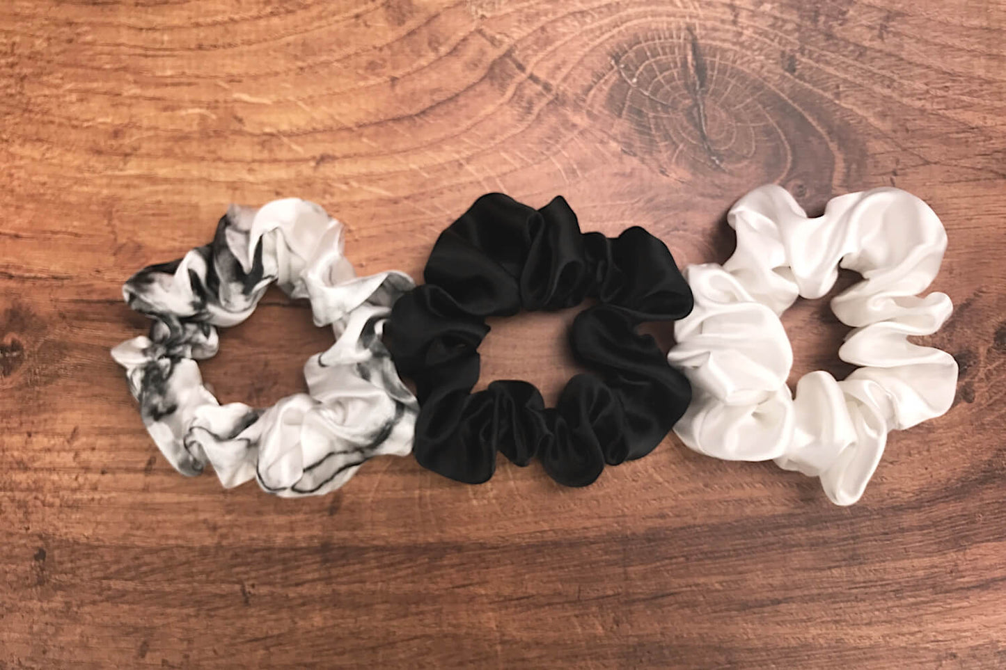 Large white marble, ivory and black silk hair ties by Celestial Silk laying side by side on a wood vanity