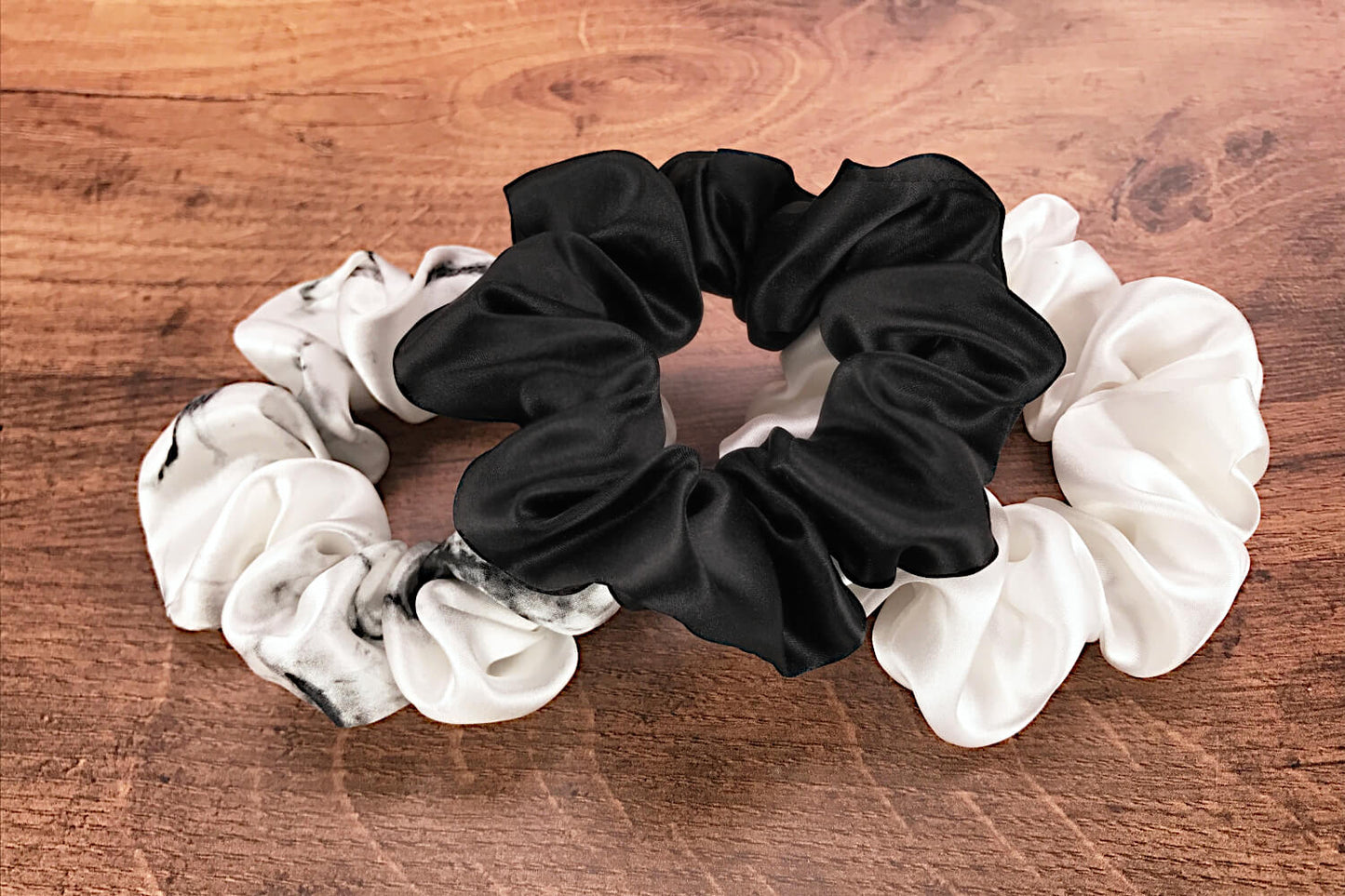 Large white marble, ivory and black silk hair ties by Celestial Silk laying in a pile on a wood vanity