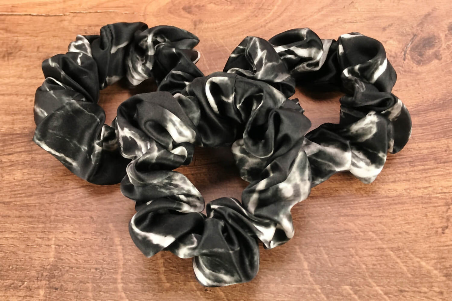Large black marble silk hair ties by Celestial Silk laying in a pile on a wood vanity