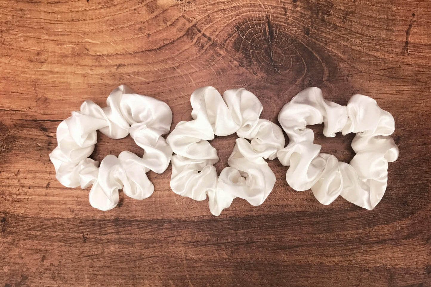 Large undyed ivory silk hair ties by Celestial Silk stacked side by side on a wood vanity