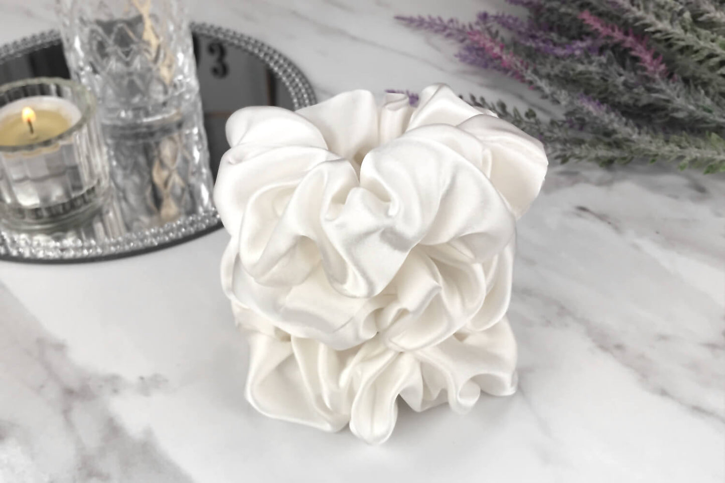 Celestial Silk large undyed ivory silk scrunchies stacked on marble counter with lavender plant and a candle in the background