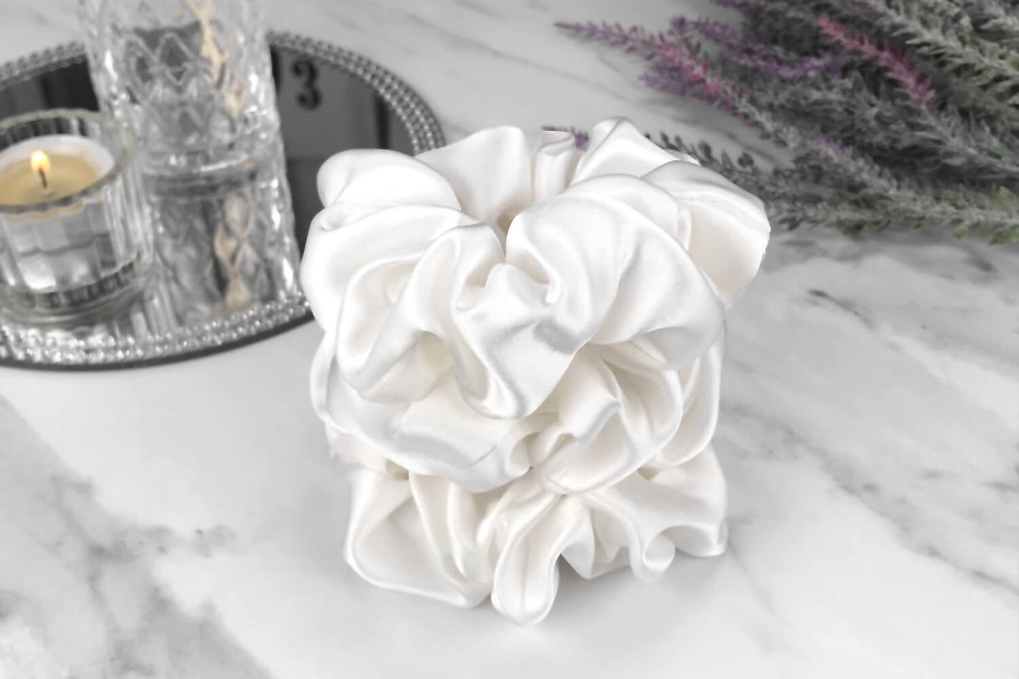 Celestial Silk large white silk scrunchies stacked on marble counter with lavender plant and a candle in the background