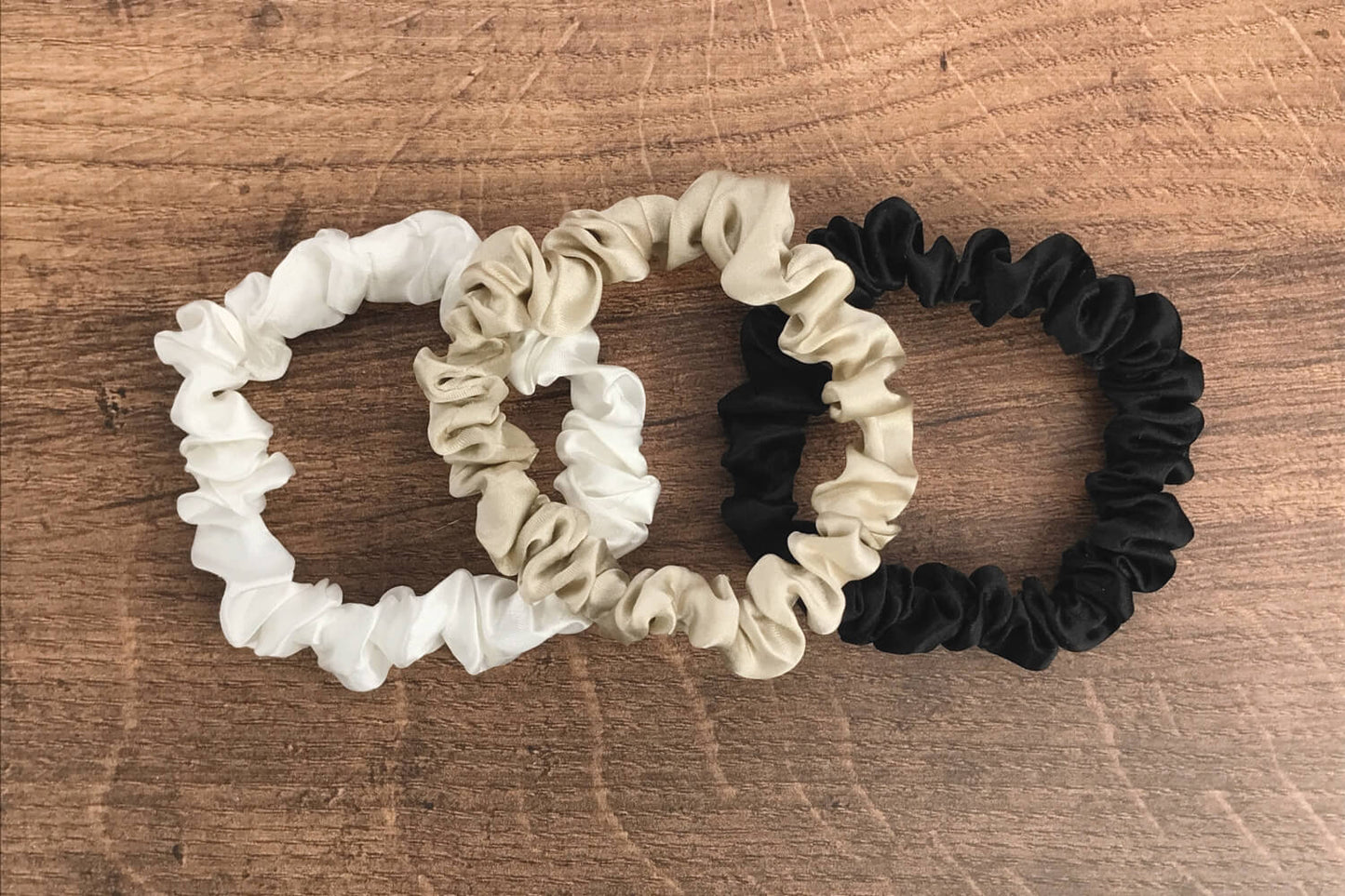 thin taupe ivory and black silk hair ties by Celestial Silk laying in a pile on a wood vanity