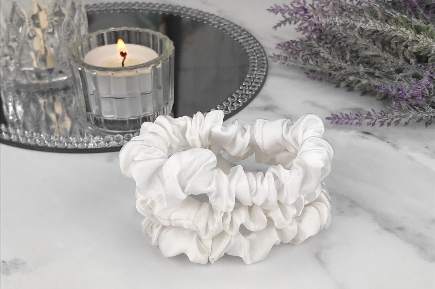 Celestial Silk skinny ivory silk scrunchies stacked on marble counter with lavender plant and a candle in the background