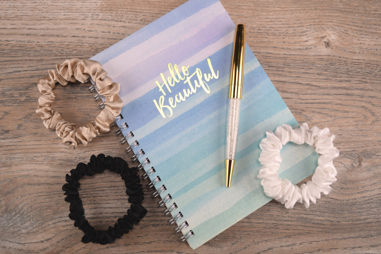thin taupe ivory and black silk hair ties by Celestial Silk laying in a pile on a wood table with notebook and pen