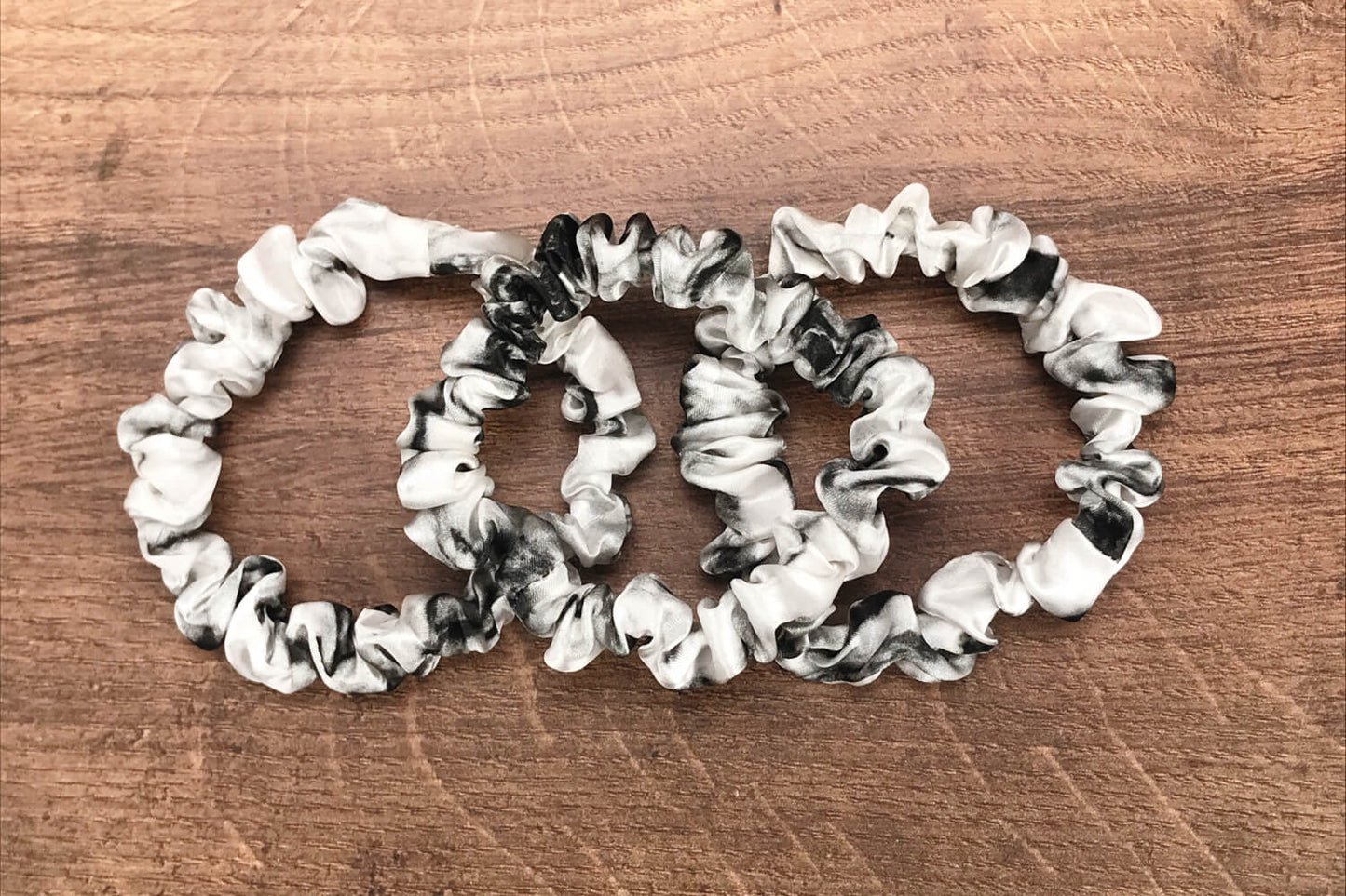 thin white marble silk hair ties by Celestial Silk laying in a pile on a wood vanity