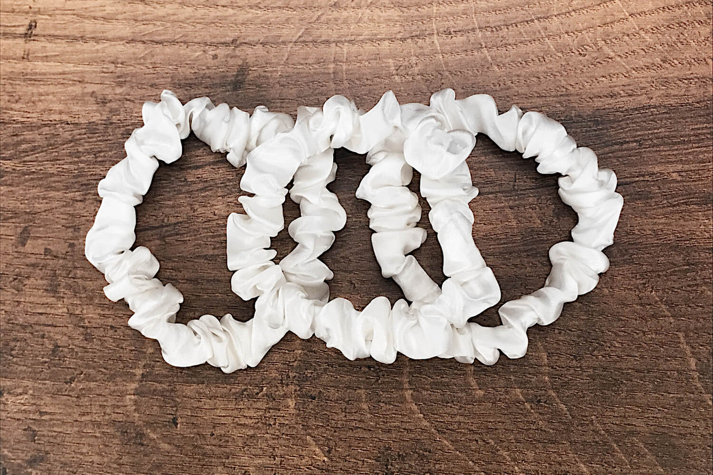 thin ivory silk hair ties by Celestial Silk laying in a pile on a wood vanity