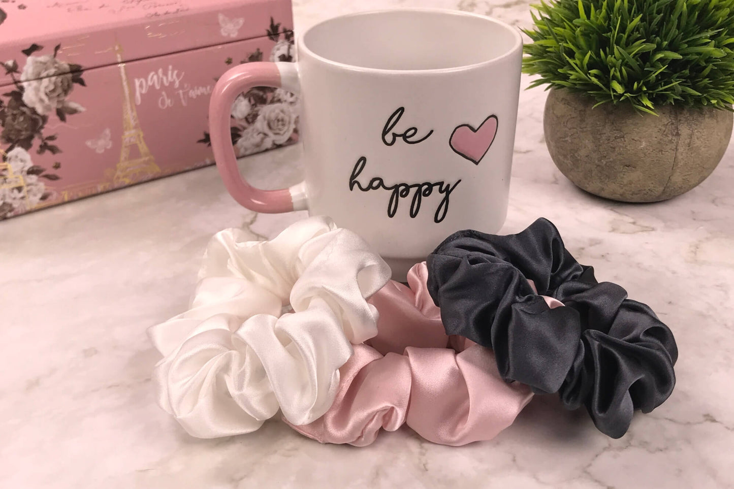 Celestial Silk large charcoal ivory and pink silk scrunchies stacked on marble counter with lavender plant and be happy cup in the background