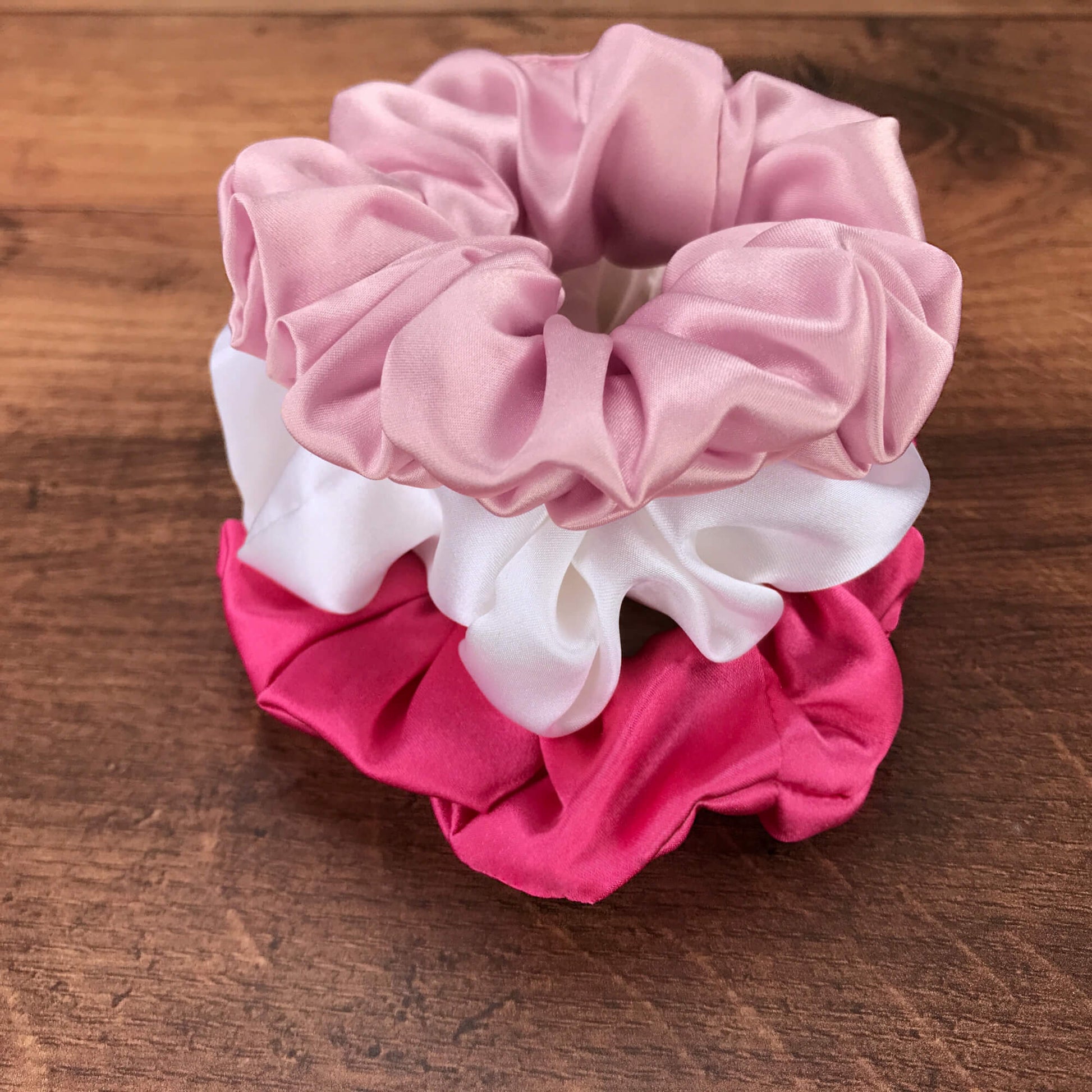 Large soft pink hot pink and white silk hair ties by Celestial Silk stacked in a pile on a wood vanity