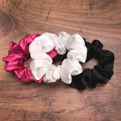 Large black hot pink and white silk hair ties by Celestial Silk laying in a pile on a wood vanity