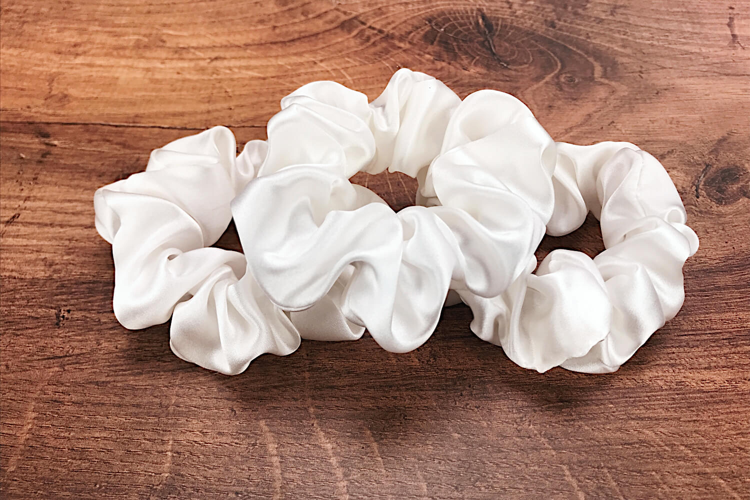 Large white silk hair ties by Celestial Silk laying in a pile on a wood vanity