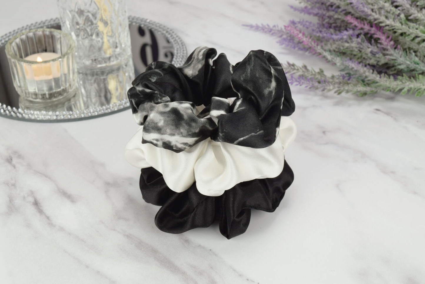 Celestial Silk large black marble, ivory and black silk scrunchies stacked on marble counter with lavender plant and a candle in the background