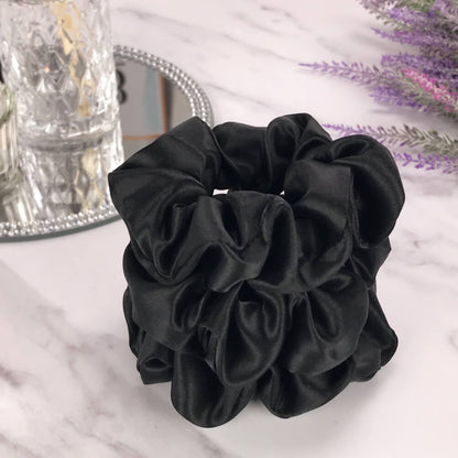 Celestial Silk large black silk scrunchies stacked on marble counter with lavender plant and a candle in the background