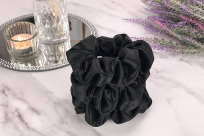 Celestial Silk large black silk scrunchies stacked on marble counter with lavender plant and a candle in the background