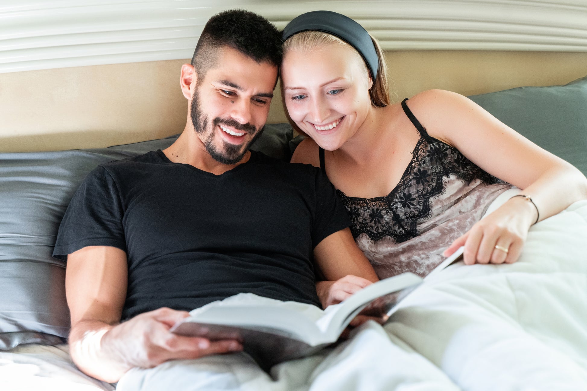 man and woman wearing silk sleeping head band reading a book together in bed