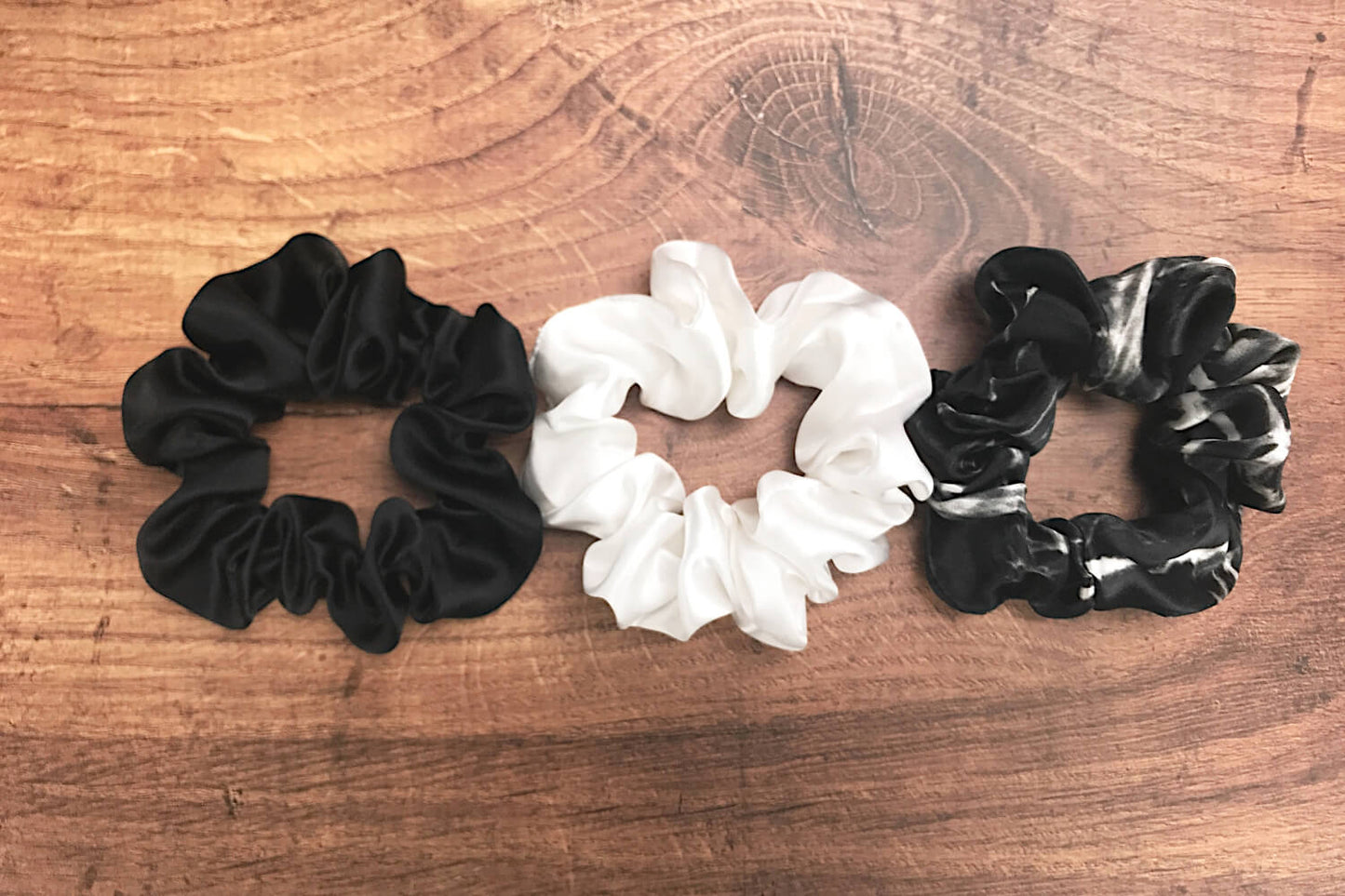 Large black marble, ivory and black silk hair ties by Celestial Silk laying in a pile on a wood vanity