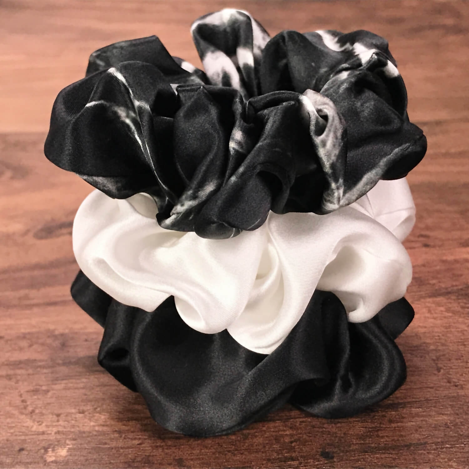 Large black marble, ivory and black silk hair ties by Celestial Silk stacked in a pile on a wood vanity