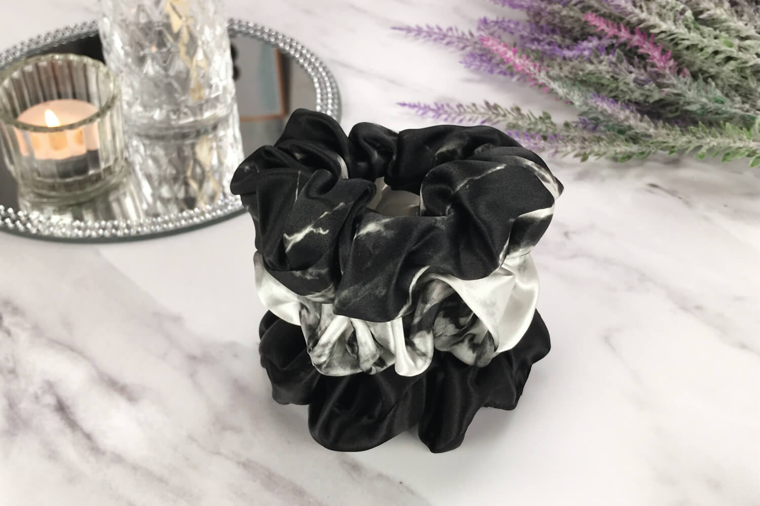 Celestial Silk large marble silk scrunchies stacked on marble counter with lavender plant and a candle in the background