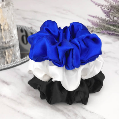 Celestial Silk large black , blue and white silk scrunchies stacked on marble counter with lavender plant and a candle in the background