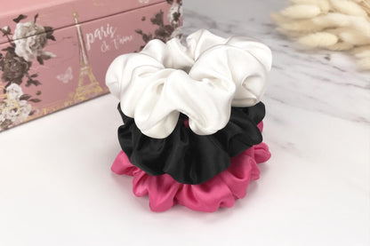 Celestial Silk large black hot pink and white silk scrunchies stacked on marble counter with plant in the background