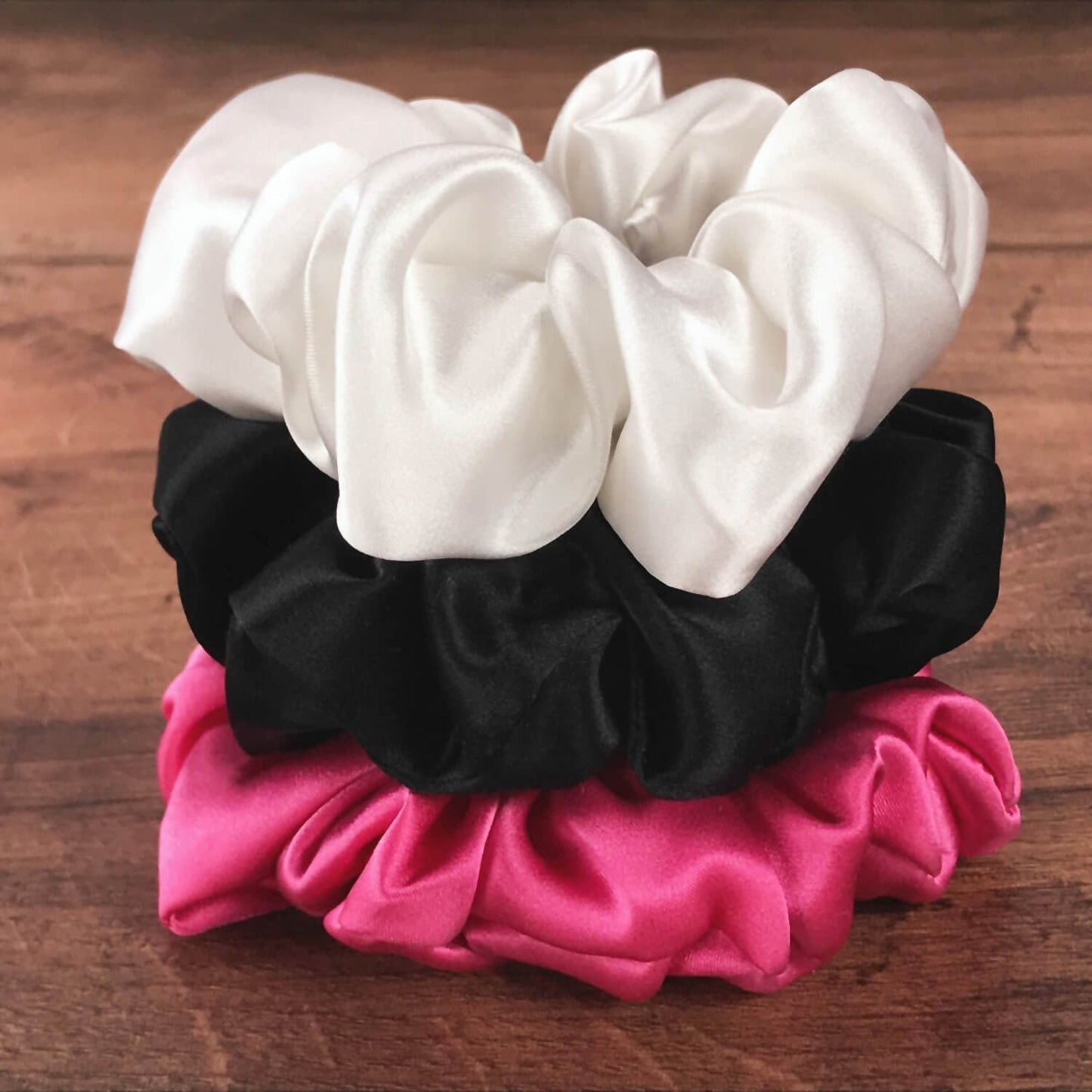 Large black hot pink and white silk hair ties by Celestial Silk stacked in a pile on a wood vanity