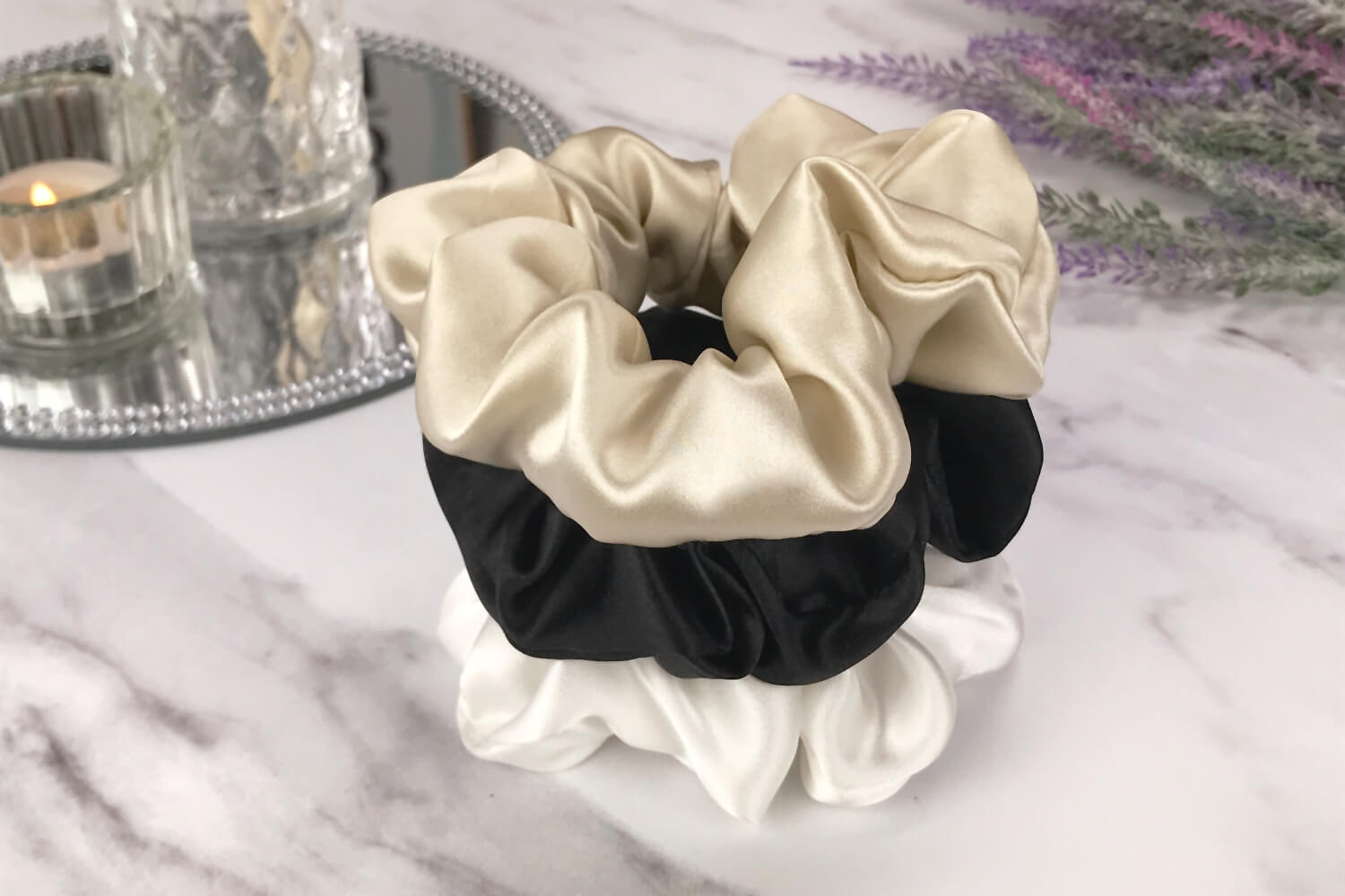 Celestial Silk taupe ivory and black silk scrunchies stacked on marble counter with lavender plant and a candle in the background