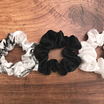 Large white marble, ivory and black silk hair ties by Celestial Silk laying side by side on a wood vanity