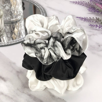 Celestial Silk large white marble, ivory and black silk scrunchies stacked on marble counter with lavender plant and a candle in the background