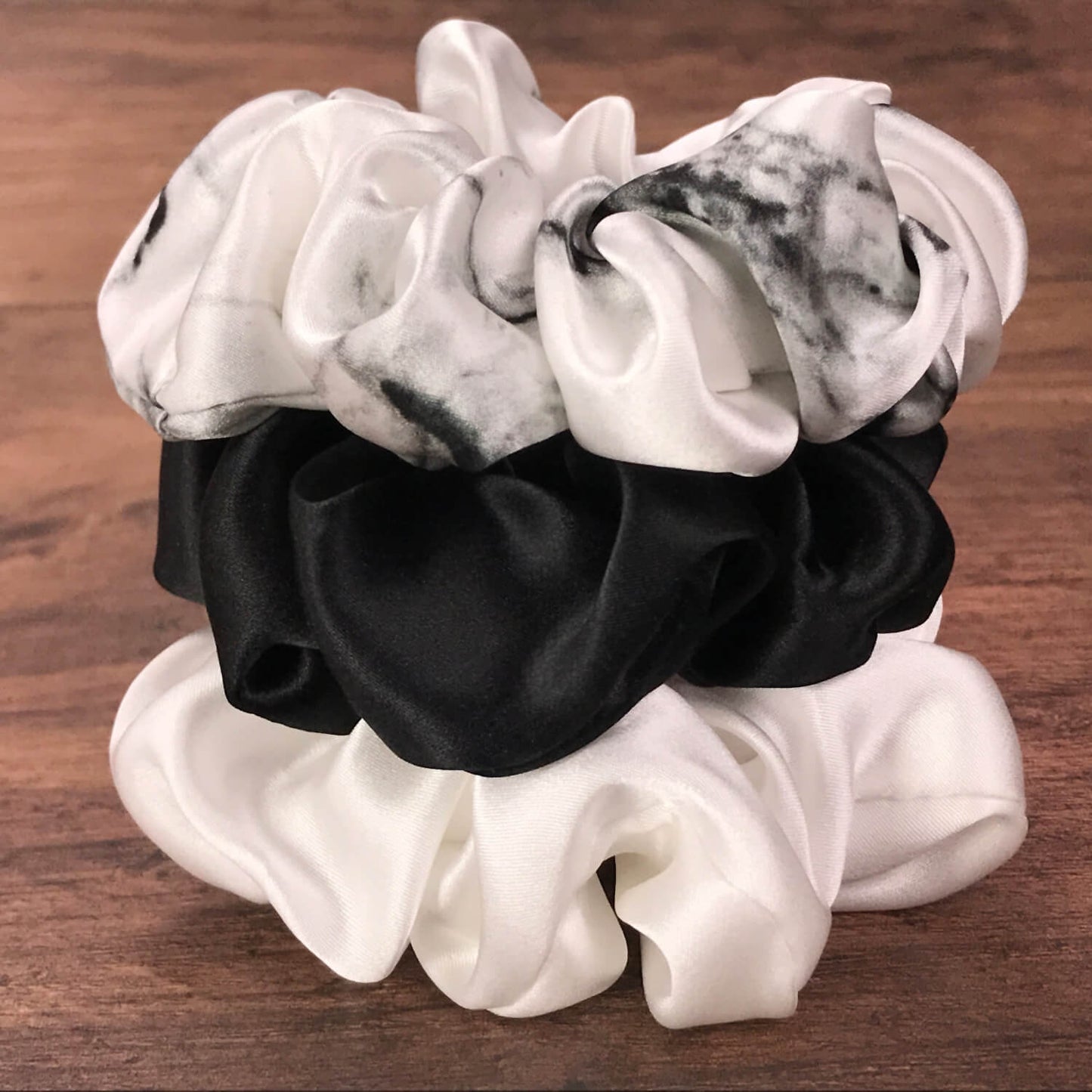 Large white marble, ivory and black silk hair ties by Celestial Silk stacked in a pile on a wood vanity