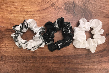 Large white marble, ivory and black marble silk hair ties by Celestial Silk laying side by side on a wood vanity