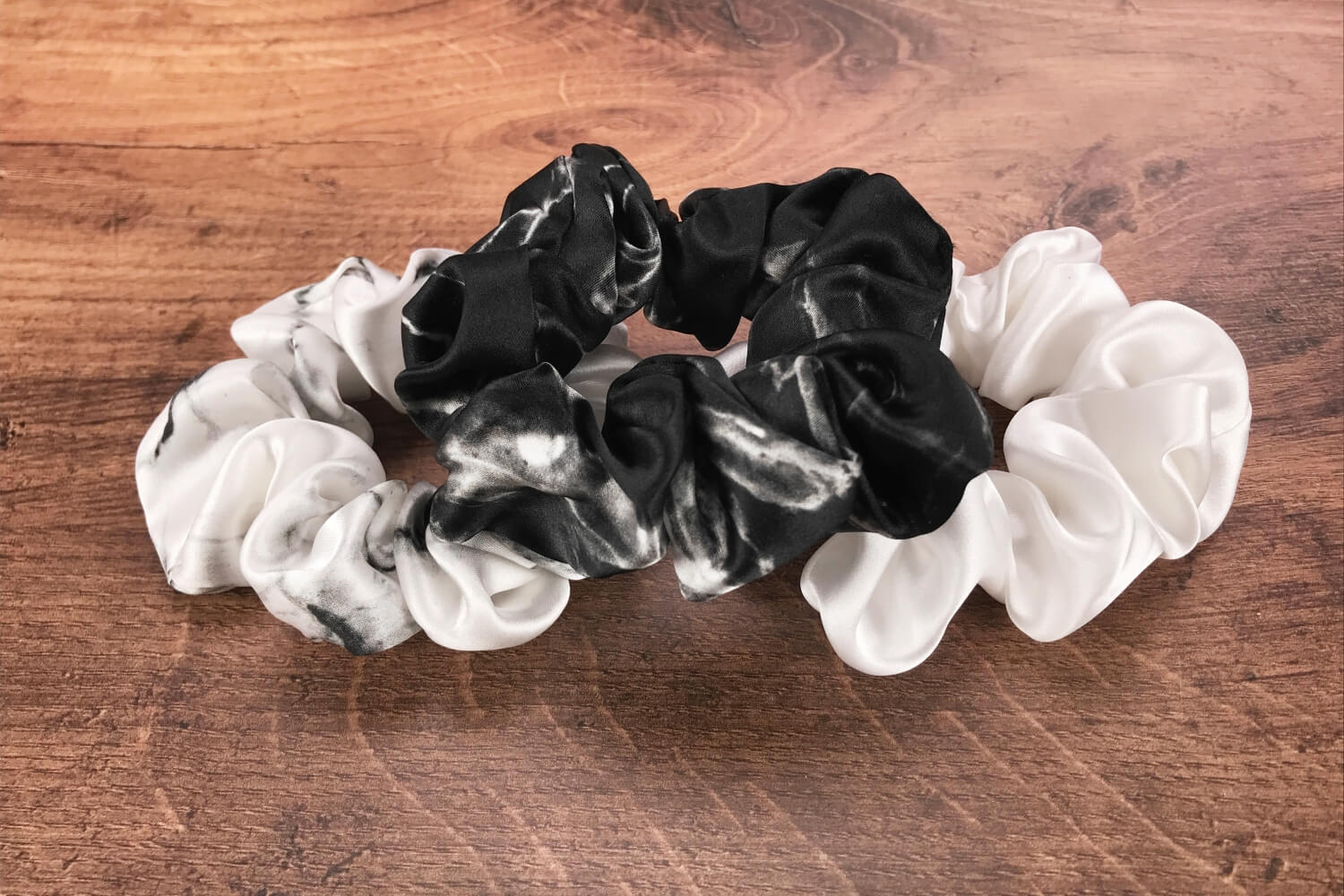 Large white marble, ivory and black marble silk hair ties by Celestial Silk laying in a pile on a wood vanity