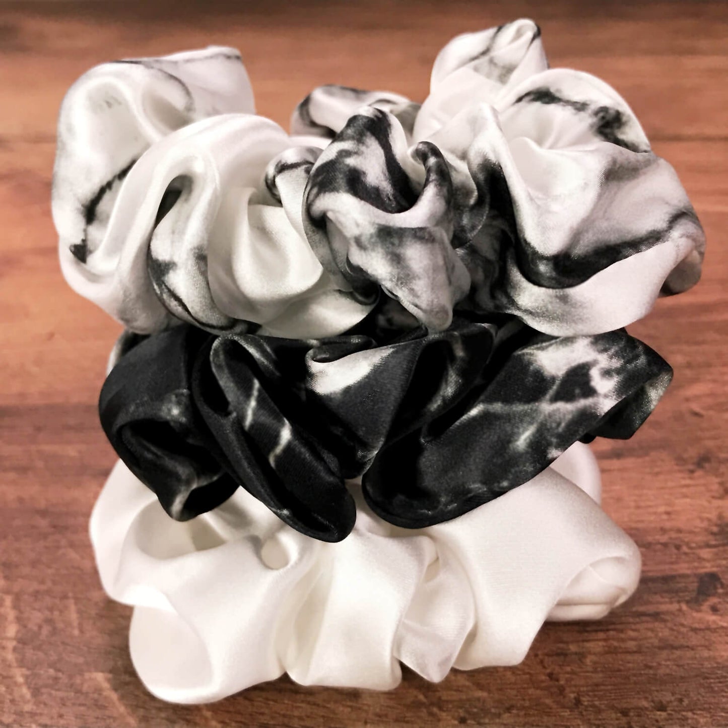 Large white marble, ivory and black marble silk hair ties by Celestial Silk stacked in a pile on a wood vanity