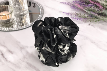 Celestial Silk large black marble silk scrunchies stacked on marble counter with lavender plant and a candle in the background