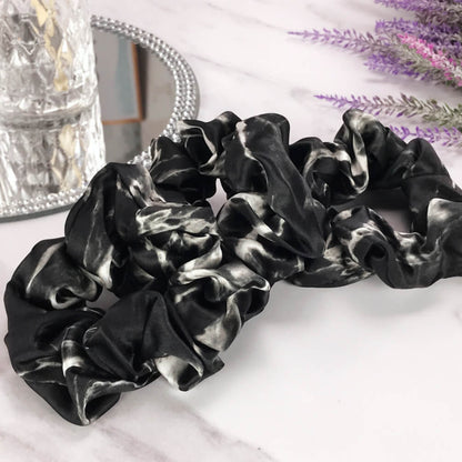 Celestial Silk large black marble silk scrunchies laying on marble counter with lavender plant and a candle in the background