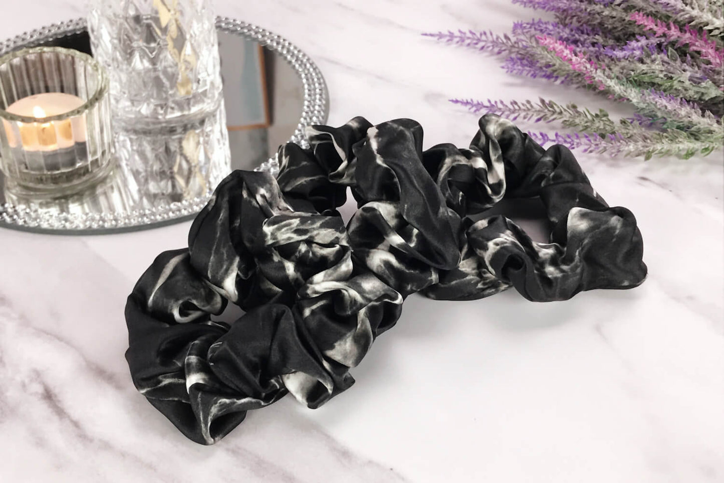 Celestial Silk large black marble silk scrunchies laying on marble counter with lavender plant and a candle in the background