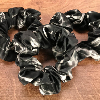 Large black marble silk hair ties by Celestial Silk laying in a pile on a wood vanity