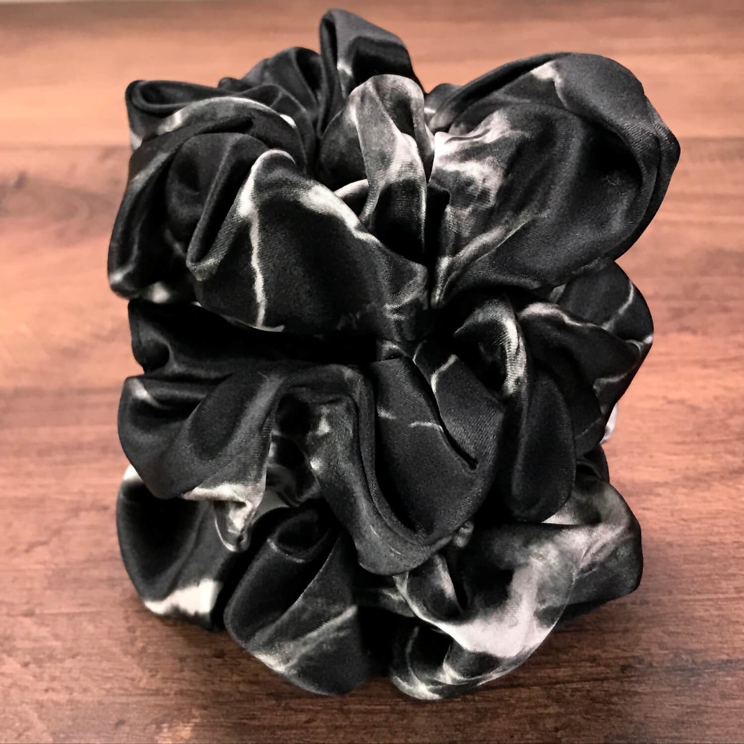 Large black marble silk hair ties by Celestial Silk stacked in a pile on a wood vanity