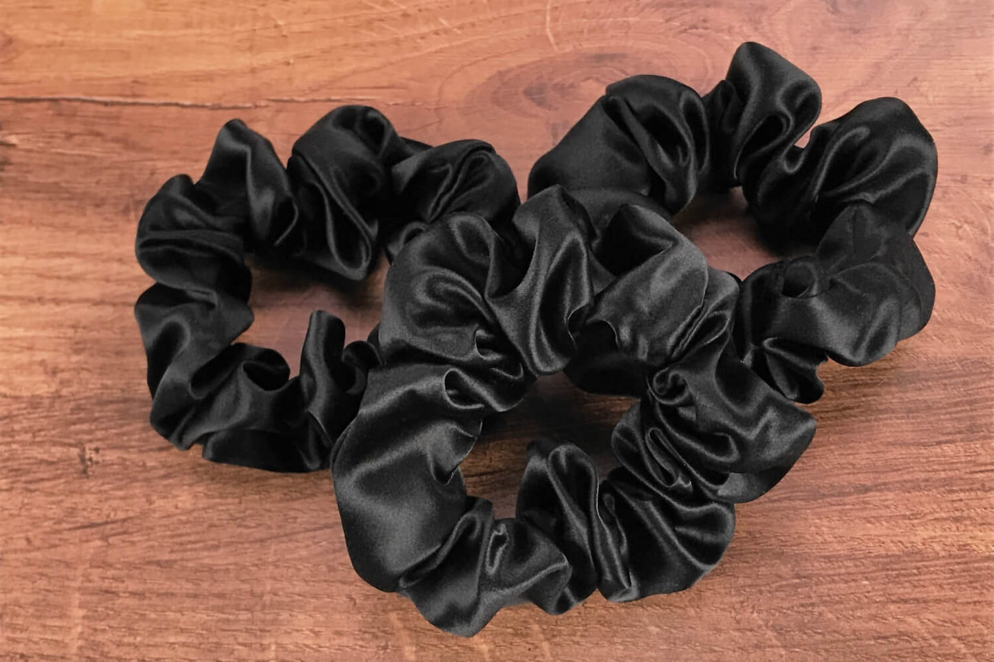 Large black silk hair ties by Celestial Silk laying in a pile on a wood vanity