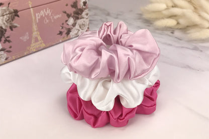 Celestial Silk large soft pink hot pink and white silk scrunchies stacked on marble counter with plant in the background