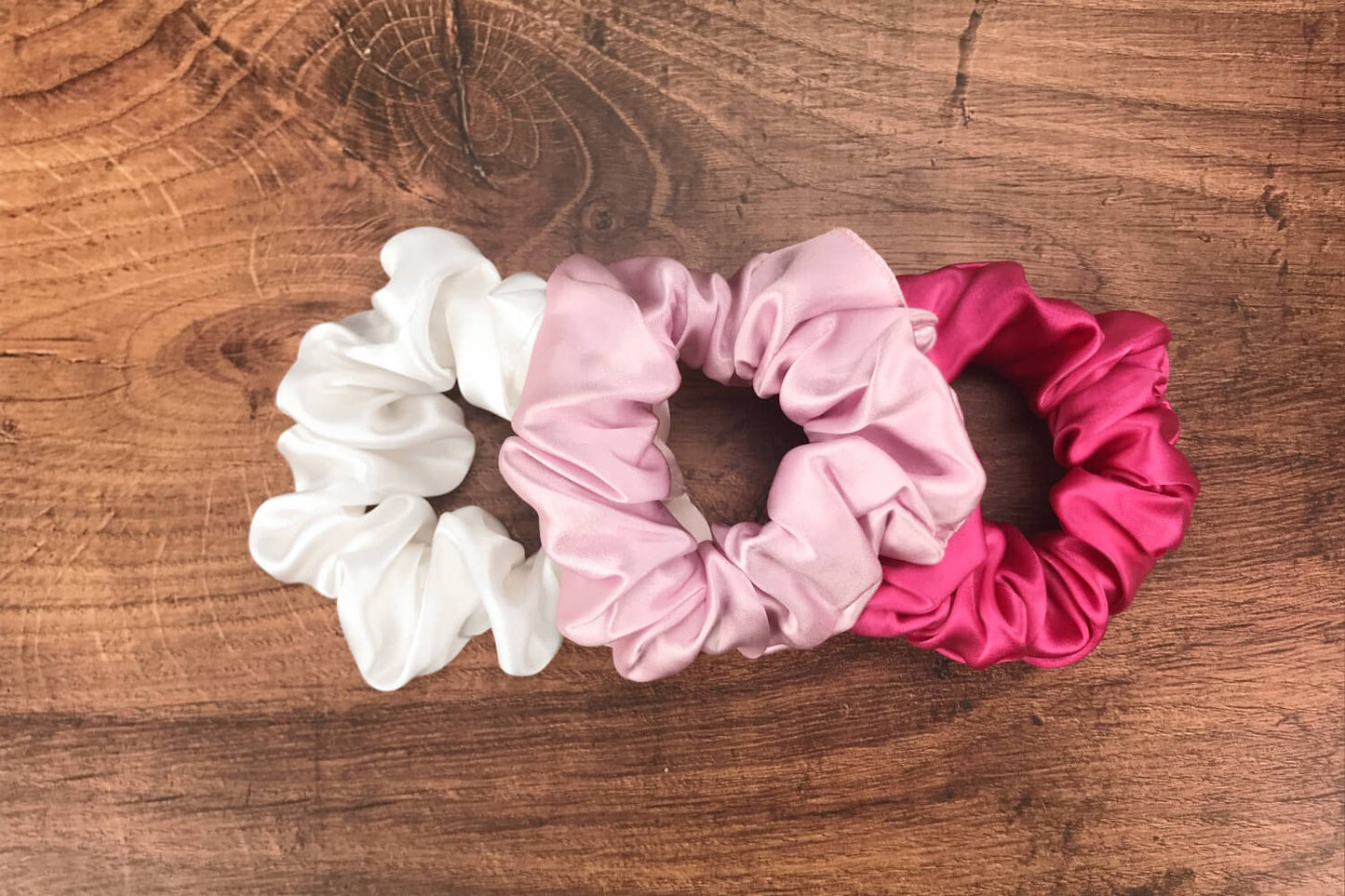 Large soft pink hot pink and white silk hair ties by Celestial Silk laying in a pile on a wood vanity