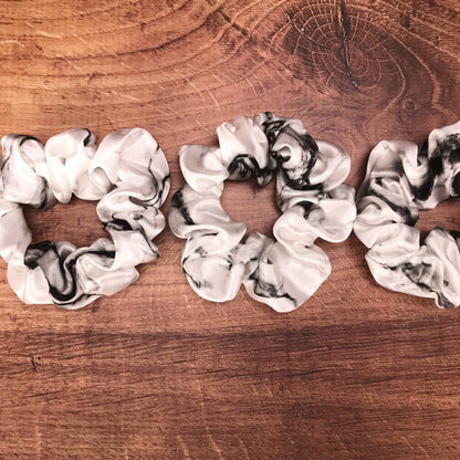 thick white marble silk hair ties by Celestial Silk laying in a pile on a wood vanity