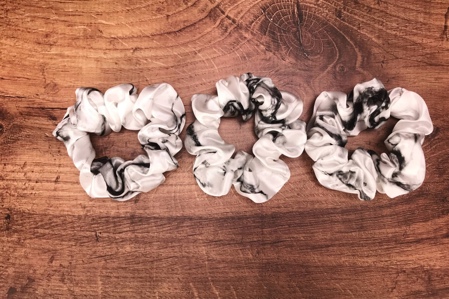thick white marble silk hair ties by Celestial Silk laying in a pile on a wood vanity