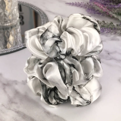Celestial Silk large white marble silk scrunchies stacked on marble counter with lavender plant and a candle in the background