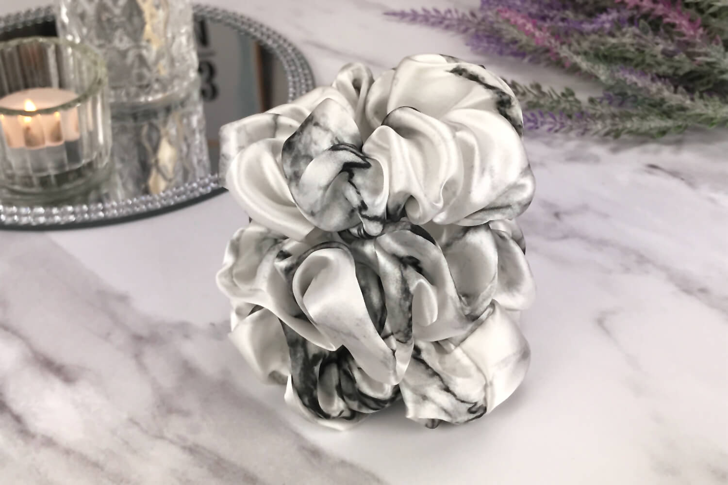 Celestial Silk large white marble silk scrunchies stacked on marble counter with lavender plant and a candle in the background