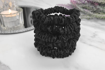 Celestial Silk skinny black silk scrunchies stacked on marble counter with lavender plant and a candle in the background