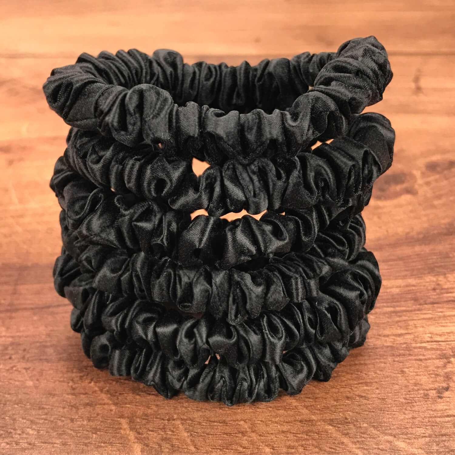 thin black silk hair ties by Celestial Silk stacked in a pile on a wood vanity