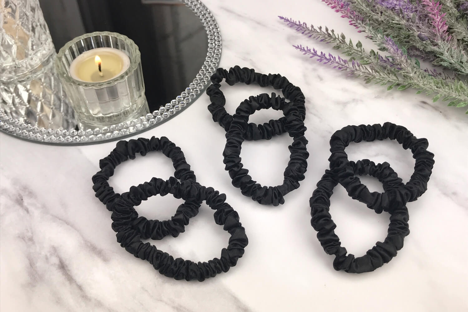 Celestial Silk skinny black silk scrunchies laying on marble counter with lavender plant and a candle in the background