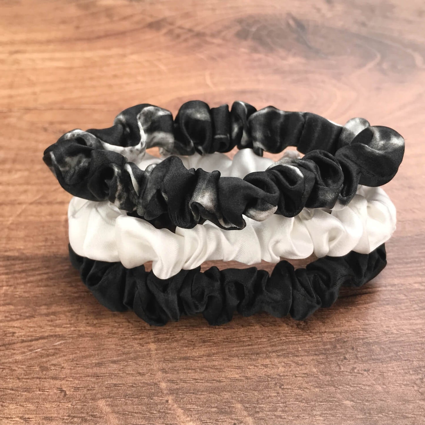 thin black marble black and ivory silk hair ties by Celestial Silk stacked in a pile on a wood vanity